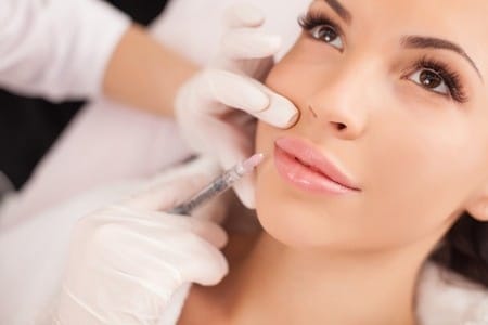 46915377 - primer plano de las manos de la cosmetóloga que realiza la inyección de botox en los labios femeninos. la joven y bella mujer está recibiendo el procedimiento con placer