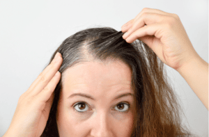 woman is checking white hair while looking at the mirror