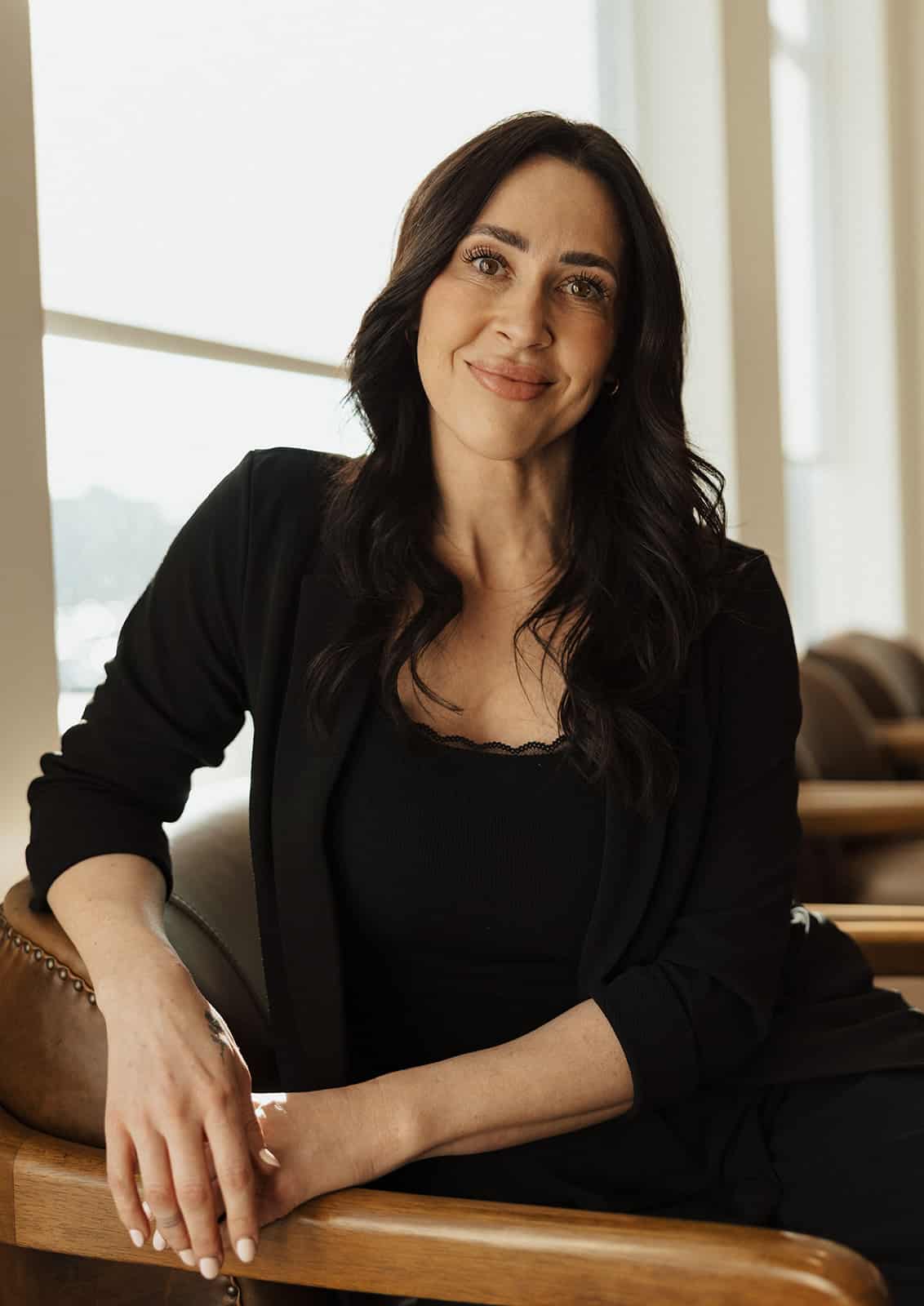 Woman with dark hair smiling while seated in a chair at Utah Facial Plastics.